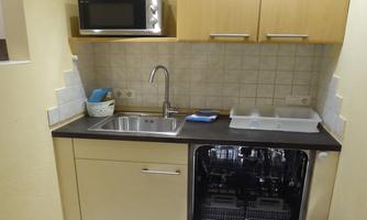 A small, modern kitchen with a sink, a microwave, and a dishwasher. The wooden fronts create a cozy atmosphere.