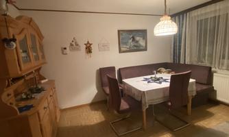A cozy dining area with a table and upholstered chairs. In the background, there are wooden shelves and a picture on the wall.