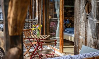 A cozy balcony with a small wooden table and chairs. On the table, there is a vase with colorful flowers, and the wooden cladding creates a warm, inviting atmosphere.
