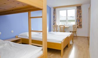 A simple room with a bunk bed and two single beds. The room has large windows that let in plenty of daylight.