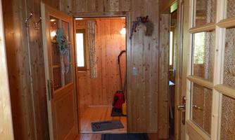 A bright hallway with wooden walls and doors. In the background, there is a vacuum cleaner, and a carpet lies on the floor.