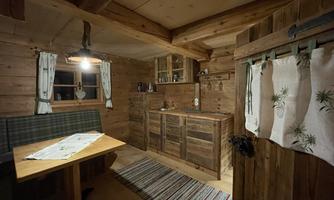 A cozy wooden cabin with a small kitchen and a dining table. The walls are made of wood and there is soft lighting.