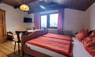 A cozy bedroom with two single beds and orange bed covers. There is a small table, a television, and large windows that let in daylight.