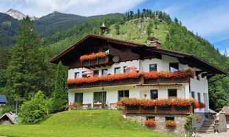 A beautiful, typical Bavarian house with colorful flower balconies. In the background, green mountains and a blue sky can be seen.