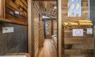 A cozy interior with wooden paneling and a clear view of a bedroom. Towels are neatly placed on a shelf.