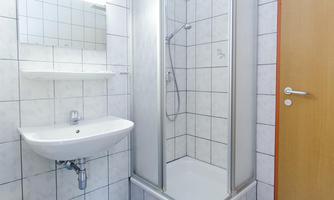 A modern bathroom with a shower, a sink, and a toilet. The tiles are light and clean.