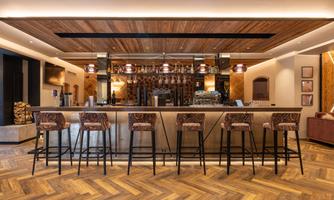 An elegant bar with wooden elements and modern stools. The room is well-lit and has a pleasant atmosphere.