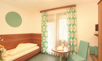 A simple room with modern furniture and colorful curtains. There is a bed, a round table, and a chair.