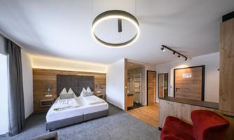 A modern hotel room with a double bed and elegant wooden paneling. The room is bright and inviting due to large windows and stylish lighting.