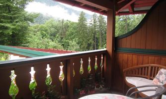 A cozy porch overlooking green trees and mountains. A floral tablecloth is on the table and a chair is ready to sit in.