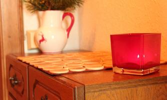 A wooden table with a set of round coasters. On it sits a red candle and a white pitcher with a deer motif.