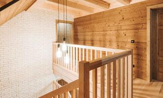 A modern hallway with wooden paneling and an elegant railing. Ceiling lamps provide warm lighting.