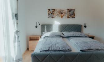 A modern bedroom with a large bed and decorative pillows. The walls are painted light, and a piece of art hangs above the bed.