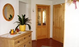 A cozy hallway with wooden details and a mirror. A green plant is in a pot on a chest of drawers, creating a warm and inviting atmosphere.