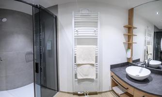 A modern bathroom with a glass shower and an elegant sink. White towels hang on a towel warmer and a wooden shelf complements the decor.
