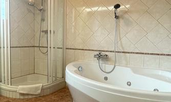 A modern bathroom with a shower and a whirlpool. The walls are tiled in light colors and the floor has a patterned design.