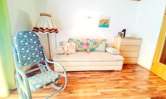A cozy room with a bright sofa and a comfortable chair. The wooden floor and the decorative elements create an inviting atmosphere.