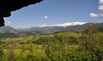 A picturesque landscape with green hills and snow-covered mountains in the background. The sky is blue with a few clouds.