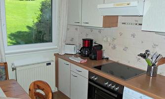 A bright kitchen with wooden features and modern appliances. Through the window, there is a view of a green lawn.