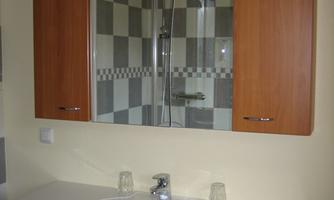 A modern bathroom with a sink and wooden cabinets. In the background, a shower with checkered tiles can be seen.