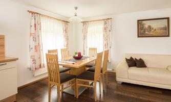 A bright dining room with a wooden table and six chairs. A cozy sofa and a painting adorn the space.