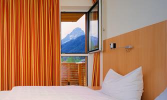 A comfortable hotel room with a window that overlooks a mountain landscape. The colorful curtains give the room a cozy atmosphere.