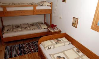 A simple bedroom with a bunk bed and a single bed. The beds are adorned with subtle bedding and pillows.