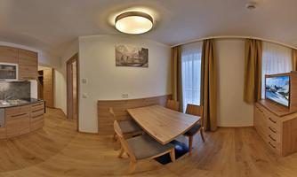 A modern apartment with an open kitchen and a dining area. Bright walls and large windows create a cheerful atmosphere.