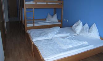 A simple room with a bunk bed and two single beds. The walls are painted blue and there are light wooden floors.