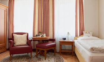 A cozy room with a single bed, a table, and two chairs. Large windows provide plenty of daylight and a pleasant atmosphere.