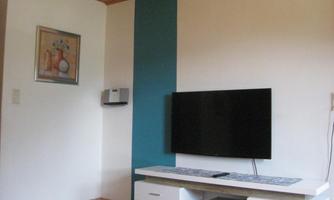 A modern living room with a large television on the wall. The walls are painted in neutral colors, with a blue accent and a small picture frame.