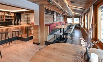 A modern restaurant with wooden interior and cozy atmosphere. There are tables and chairs as well as an adjoining bar.