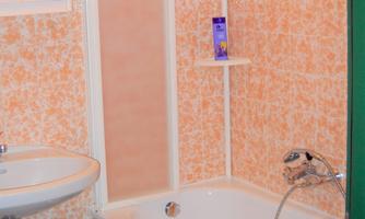 A bathroom with a bathtub and a shower cabin. The walls are decorated with orange tiles.