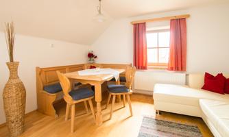 Bright living room with a dining table and chairs. The windows are decorated with red curtains and there is a cozy couch.
