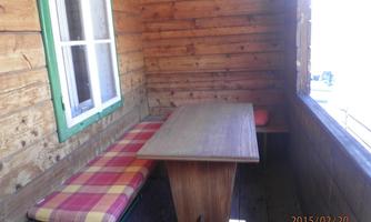 A cozy balcony with wooden walls. There is a table and a bench with checkered upholstery.