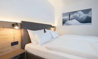 A modern bedroom with a cozy bed and white pillows. On the wall, there is a piece of art featuring a mountain landscape.