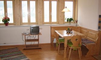 A cozy dining area with a wooden table and seating area. Large windows provide plenty of natural light and an inviting atmosphere.