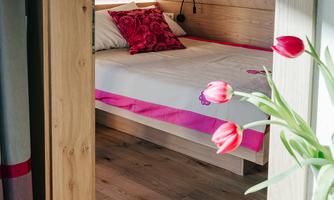 A cozy bedroom with a double bed and colorful pillows. Fresh tulips in a vase are in the foreground.