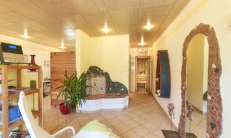 An inviting room with bright walls, a comfortable lounge chair, and plants. In the center, there is a decorative fountain installation.