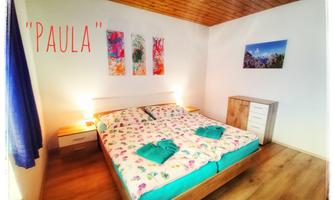 A cozy bedroom with a large bed and colorful bedding. Colorful pictures hang on the wall, and there is a modern dresser.