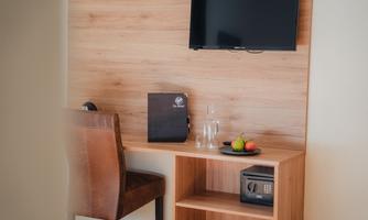 A modern room with a wooden shelf, a television, and a desk. On the table, there are water, a folder, and a fruit bowl.
