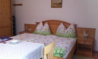 A cozy bedroom with a double bed and colorful pillows. A table with chairs and a small picture on the wall complete the room.