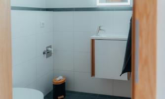 A modern bathroom with a toilet and a small sink. The walls are tile-colored and the floor is dark.