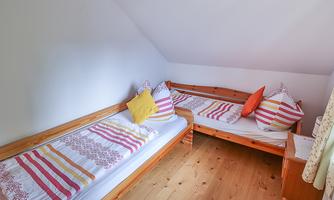 A simple room with two wooden benches and colorful cushions. The floor is made of wood and the walls are painted light.