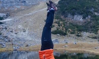 A person is doing a handstand in nature. In the background, mountains and a clear lake are visible.