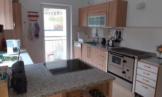 A modern kitchen with wooden cabinets and granite work surfaces. There is an open window front that lets daylight in.