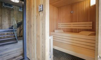 A modern sauna room with wooden paneling and comfortable loungers. In the background, a staircase can be seen.