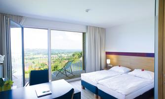 A modern room with two beds and a table. Large windows offer a view of the landscape and the balcony.