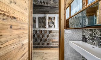 A modern bathroom with wooden paneling and stylish tiles. The decor is bright and welcoming, featuring a sink and large windows for natural light.
