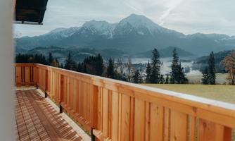 A beautiful view from a balcony of snow-covered mountains and green forests. The landscape radiates tranquility and a connection to nature.